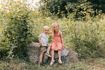 The Sage kids sitting together on a rock among blooming flowers and tall grass.