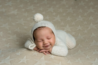 Newborn baby in white outfit smiling during studio newborn session near New Canaan, CT