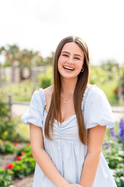 Texas A&M senior girl laughing at camera in blue dress at Leach Teaching Gardens