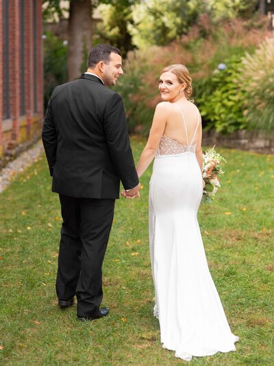 Bride looks over her shoulder as her husband holds her hand.