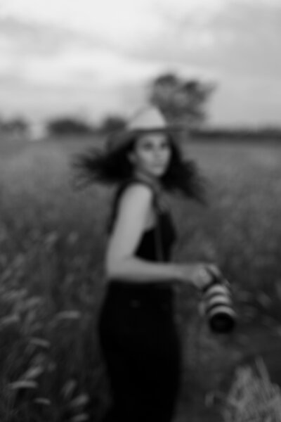 woman walking through a field in a cowboy hat holding a camera