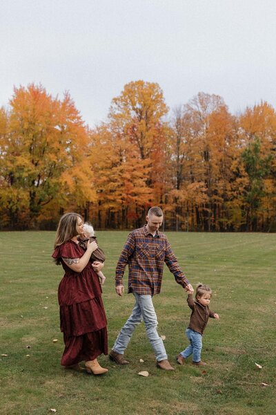 Family of four walking through a Cleveland park surrounded by vibrant fall foliage during a mini session