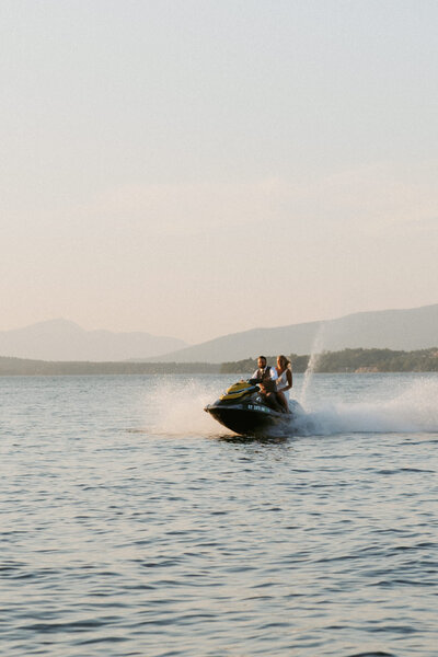 a bride in a wedding dress riding a jetski during her elopement on Lake Winnipesaukee in New Hampshire at sunset