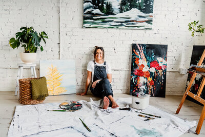 a woman artist, painter sitting in a tacoma studio with her paintings around her for a branding photo shoot