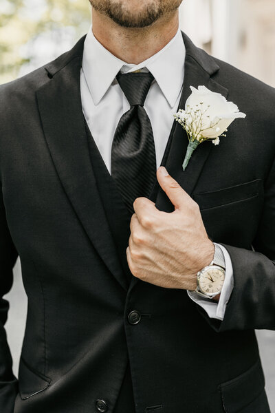 Close-up of groom in a black suit and white boutonniere adjusting his jacket, captured at Ashford Acres Inn.
