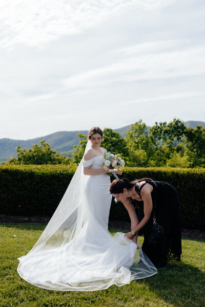 photo of west virginia wedding photographer helping to straighten out bride's dress