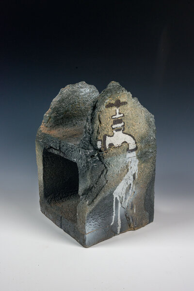 A cinder block that was hand made out of clay is decorated with underglaze to resemble graffiti and various other imagery