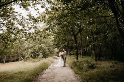 Een romantisch bruidspaar poseert in het bos met veel groen in de omgeving.