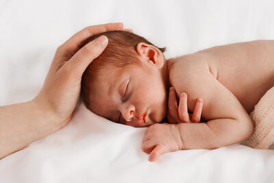Newborn in a soft pose with arms tucked under the head, wearing a neutral-toned bonnet. Photographed with gentle elegance by Sophie Louise.
