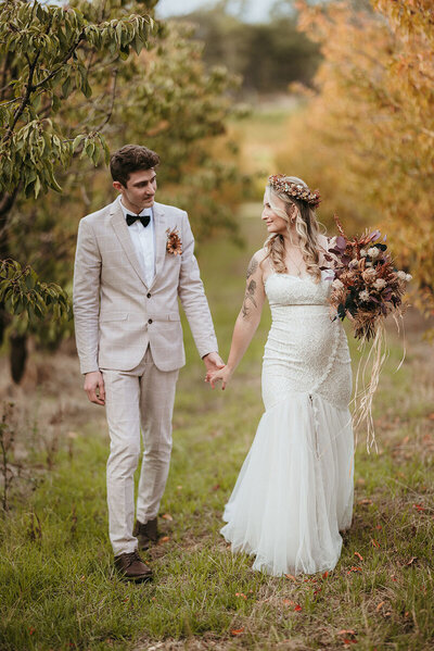 Bride and groom in an orchard, bride is smiling and holding her flower bouquet
