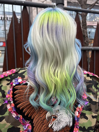 Image of client with bleach blonde hair that has highlights and lowlights of blue, green, and purple.