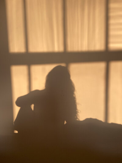 Silhouette of a person sitting by a window, casting soft shadows. The warm light creates a serene and contemplative atmosphere.