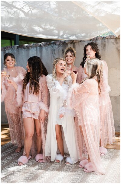 bride toasts her bridesmaids surrounding her as they get ready for the bride's big day