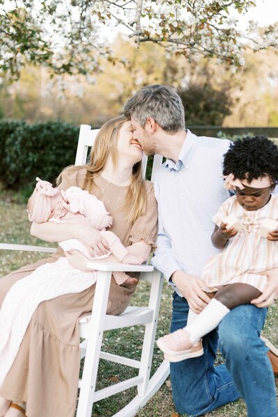 mom and dad kissing while holding their children during peoria, illinois outside newborn photos 