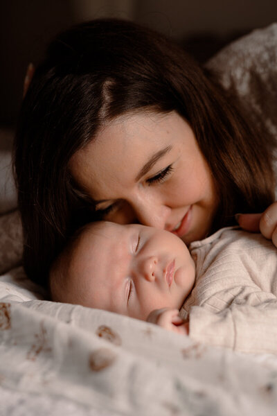Moeder ligt naast haar baby op bed en ruikt aan de wang van de baby.