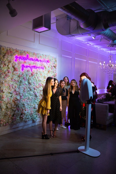 Salsa photo booth in front of flower wall with group of girls taking a photo at an event