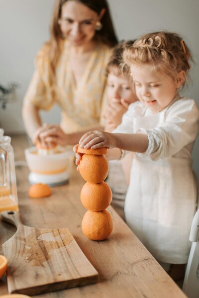 A mom and her two young children squeezing oranges. 