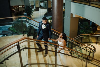 Bride and groom in elegant black-tie attire walking hand in hand on the grand staircase at the Hilton Bellevue, captured by Seattle wedding photographer Candace Connor.