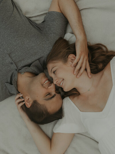 A close-up photo of a couple in the park in western new york. They are laying on a picnic blanket in opposite directions with heads touching. they are each reaching up to hold each other's face. Photo by Dash and Boheme Photography. 