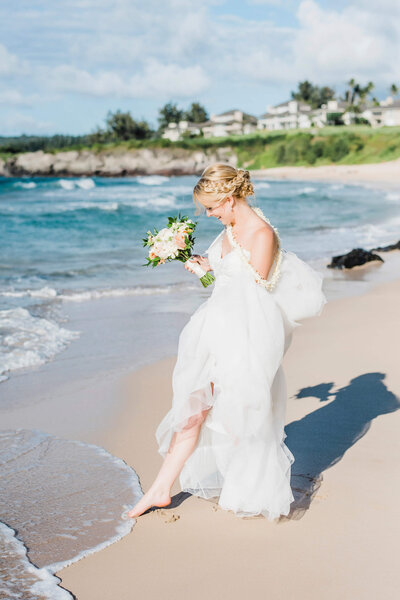 photo of a bride holding a bouquet dipping her toes in the sea, on the beach