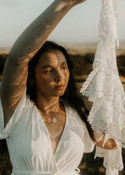 Photo of a senior girl holding up a lace blanket and casting a shadow onto her face for a cool effect.