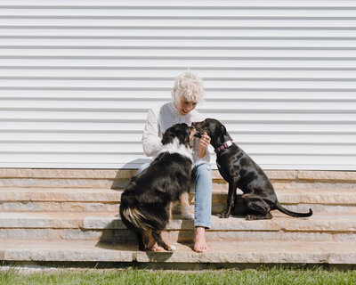 Canine bahaviorist, Sasha Armstrong, sitting on steps petting two affectionate dogs