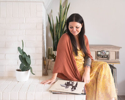 woman in earthy looking clothing sitting near a white fire place looking at records