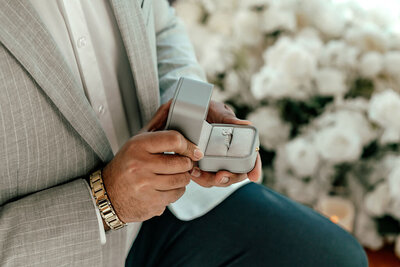 Helicopter proposal photography with couple flying above New Zealand landscape and groom holding engagement ring box, captured by Zanthe Vorsatz.