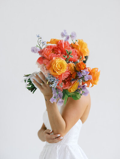 Bride holding colorful bouquet in front of her face