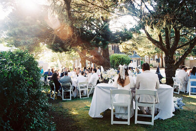 A bride and groom seen from behind at their table, as captured on film Oregon wedding photographer Among the Oaks. 