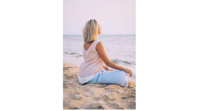 Frau sitzt im Sand am Meer und meditiert in Ruhe und in Frieden.