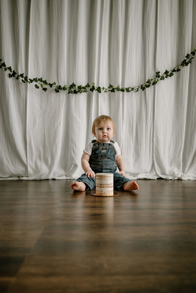 Cake Smash photo taken in a natural light studio in Annapolis Maryland with baby in denim overalls.