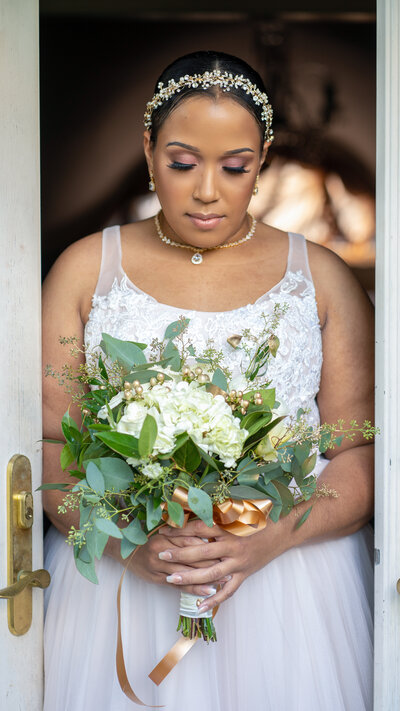 Bride stands in doorway and looks down at bouquet