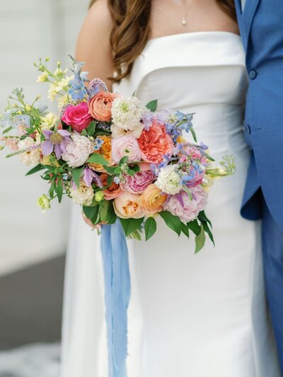 Close-up of colorful bridal bouquet with peach, coral, pink, and blue blooms