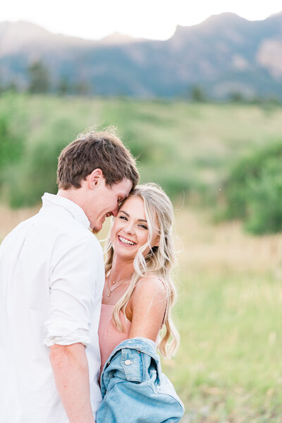 denver wedding photographer captures denver couples photography of man and woman holding hands down at their sides while the man leans into the woman as the woman smiles at the camera as they pose in a field together