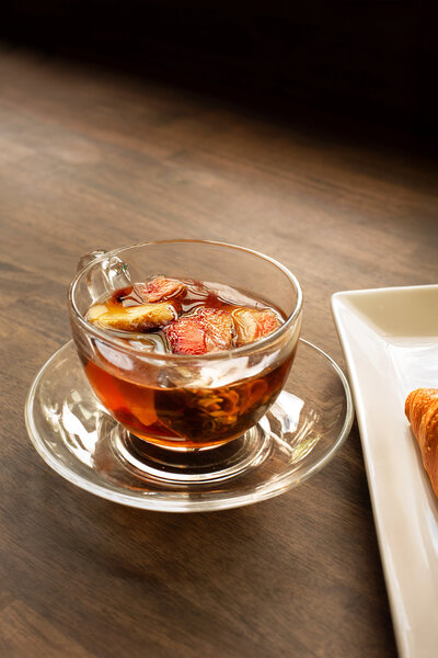 tea in clear glass cup with fruit in it on wooden surface