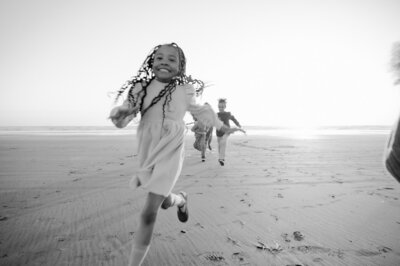 young girl in a knit dress runs joyfully from big brothers on the beach in seattle