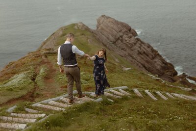 bride leads groom down trail toward a sea cliff on the East Coast Trail in Newfoundland