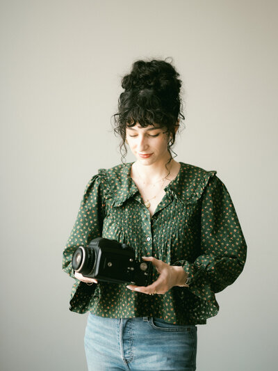 huntsville photographer holds camera wearing off the shoulder top in huntsville photography studio