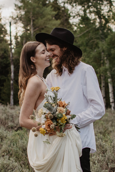 wedding portraits captured by jackson hole wedding  photographer with bride and groom embracing and laughing together in the woods