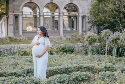 Pregnant woman in blue dress smiles in lavender garden at Eolia Mansion
