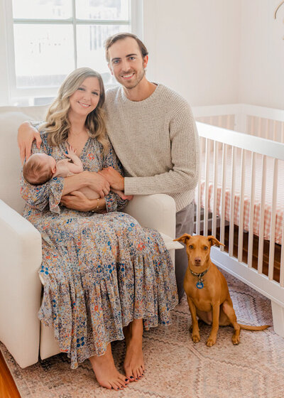 Mom holding newborn and Dad smiling with the family dog
