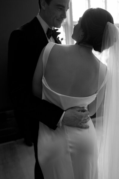Black-and-white image of bride and groom embracing in ceremony space.