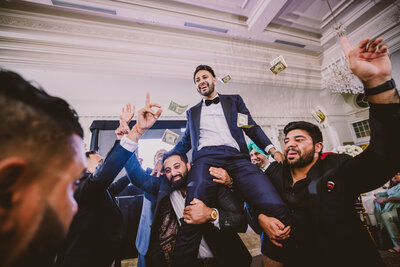 Groom being carried by guests during the wedding reception dance floor with money being thrown in the air