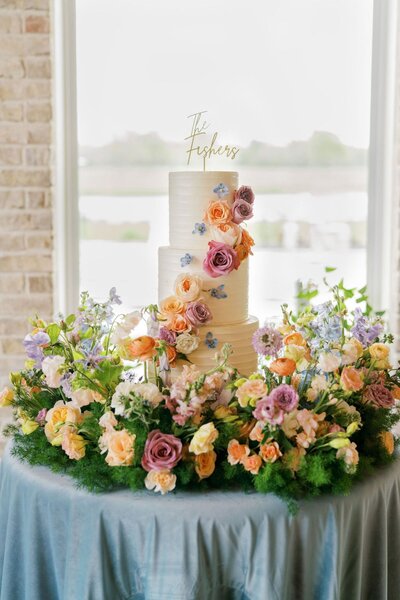 Wedding cake with cascading peach, lavender, and blush florals on garden-style base
