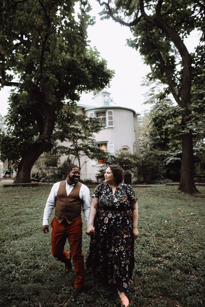 A couple walks together on the lawn outside a beautiful estate