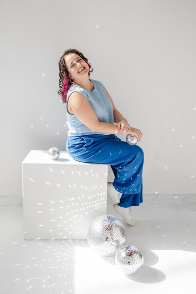 woman sitting on a white block surrounded by shimmering disco balles