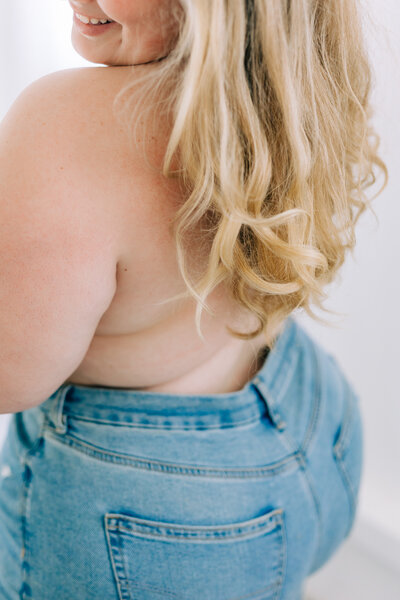 blonde woman glances over shoulder in blue jean boudoir portrait by winx photo knoxville boudoir photographer