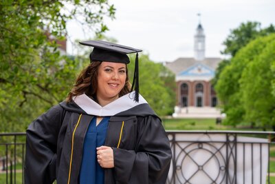 Woman dressed in her master's program cap and gown poses with one of the Johns Hopkins University's buildings behind her. Baltimore, Maryland