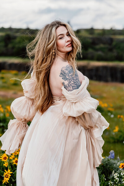 a pregnant mama looking back while walking in a field  of wildflowers in oregon